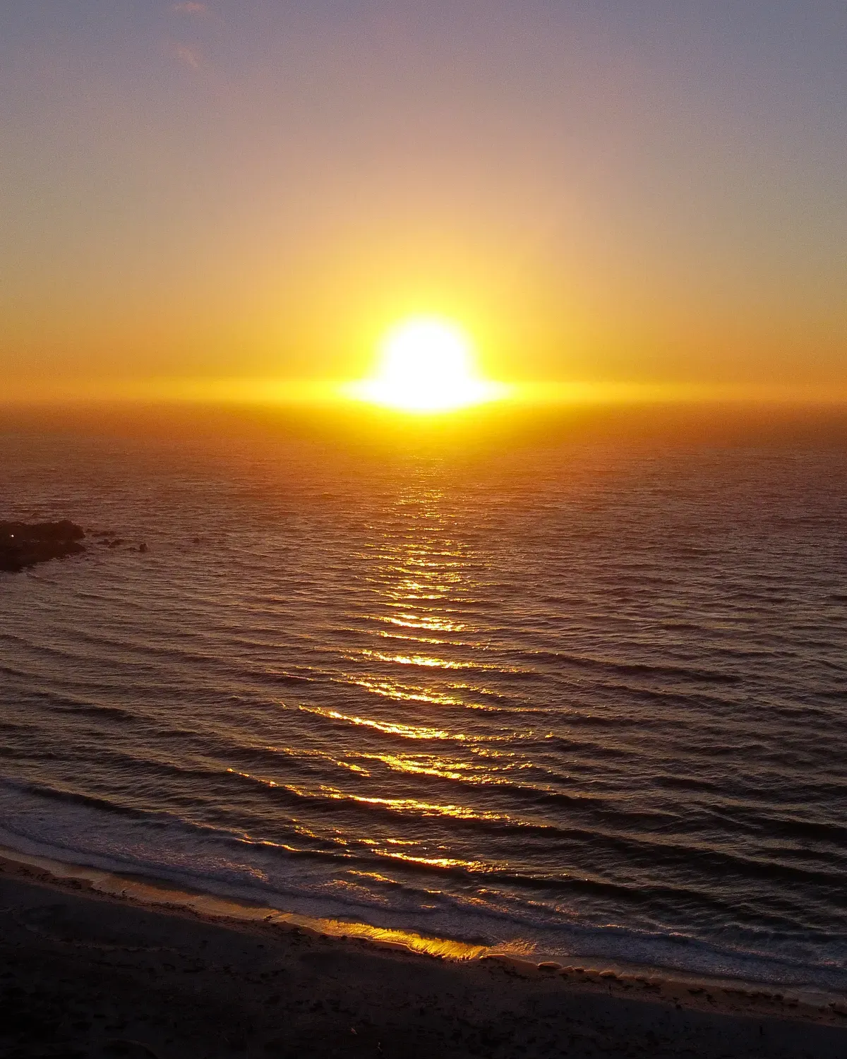 Le soleil posé sur l'horizon au-dessus de l'océan, sa lumière étalée à plat sur l'eau